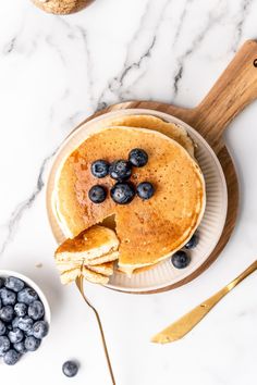 a pancake topped with blueberries on top of a white plate next to a bowl of blueberries