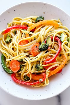 a white bowl filled with pasta and veggies on top of a marble table