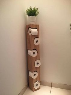 a tall wooden shelf with rolls of toilet paper on it and a potted plant in the corner