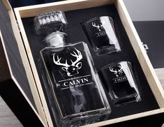 an open wooden box with three bottles and two shot glasses in it that have deer head decals on them