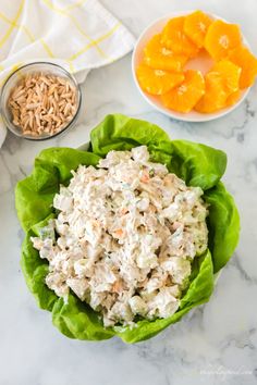 chicken salad in lettuce leaves on a marble countertop with bowls of rice and oranges