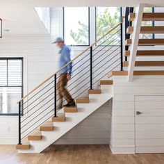 a man is walking up the stairs in a house with white walls and wood floors