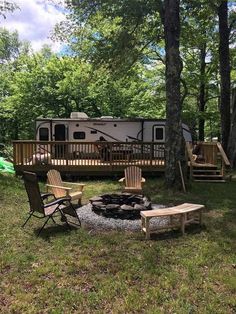 a camper sits in the woods next to a fire pit with chairs around it