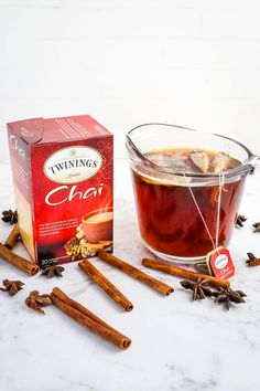 a cup of tea next to cinnamon sticks and an open box of twinings chai