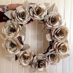 a hand holding a wreath made out of old book pages with flowers on the front