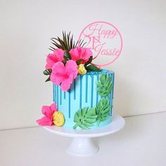 a blue cake decorated with pink flowers and palm leaves