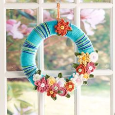 a yarn wreath hanging on a window sill in front of a flowered window