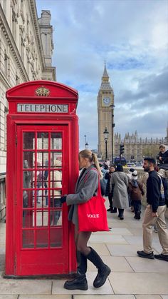 a woman is standing next to a red phone booth