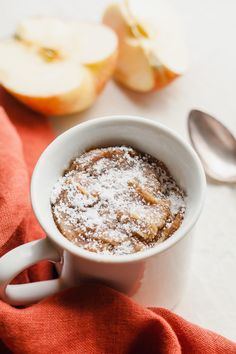 a bowl of food with powdered sugar on top next to two spoons and an apple