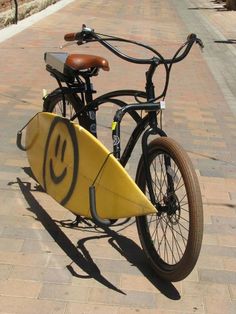 a bicycle with a surfboard attached to the front wheel is parked on a brick sidewalk