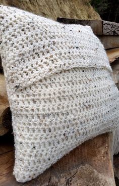 a white knitted pillow sitting on top of a pile of wood