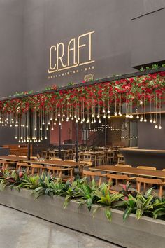 the outside of a restaurant with tables and chairs covered in hanging lights, plants and flowers