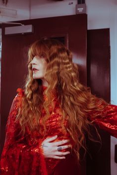 a woman with long red hair standing in front of a door wearing a red dress