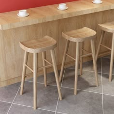 three wooden stools in front of a counter with cups on it and one is empty