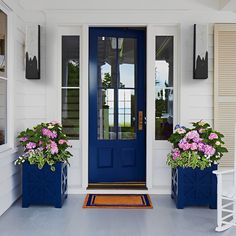 two blue planters with pink flowers on the front porch next to a blue door