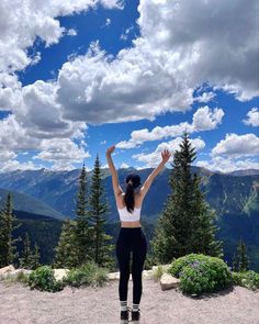 a woman standing on top of a mountain with her arms in the air