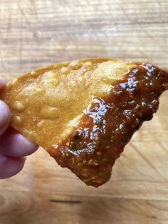 a hand holding a piece of food on top of a wooden table