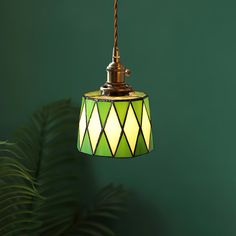 a green lamp hanging from a ceiling next to a potted plant and a wall