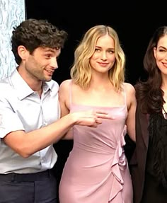 three people standing next to each other in front of a black background and one person wearing a pink dress