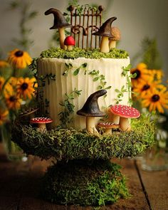 a cake decorated with mushrooms and plants on top of a wooden table next to sunflowers