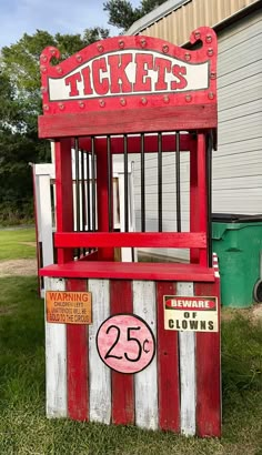 an old fashioned red and white ticket booth sitting in the grass next to a building