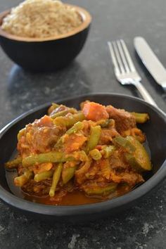 a bowl filled with meat and vegetables on top of a table next to a plate of rice