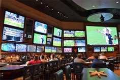 several people sitting at tables watching televisions in a sports bar with many screens on the wall