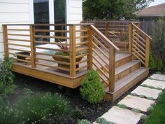 a wooden deck in front of a house with plants on it and steps leading up to the door