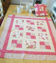 a table with a pink and white quilt on it's center, along with two cups