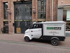 a small white and black van parked on the side of a street in front of a brick building