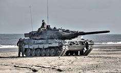 two men standing in front of a tank on the beach