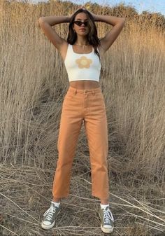 a woman standing in a field with her hands behind her head and wearing sunglasses on