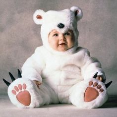 a baby dressed in a white bear costume sitting on the ground with its paws up