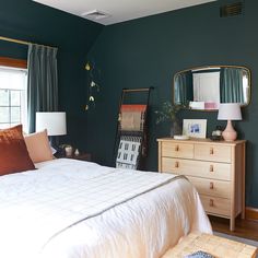 a bedroom with green walls, white bedding and wooden dresser in front of the window