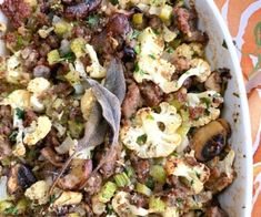 a dish filled with vegetables and meat on top of a table cloth next to utensils