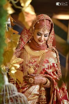 a woman dressed in red and gold is looking down at her wedding dress, while she holds