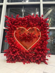 a heart - shaped sculpture made out of red flowers in front of a large window