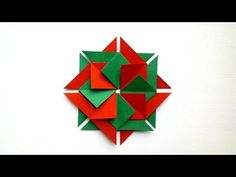 an origami flower made out of red and green paper on a white wall