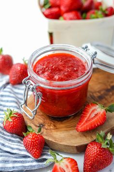 a jar of strawberry jam sitting on top of a cutting board next to strawberries