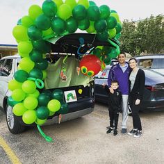 two adults and a child standing in front of a car with balloons on the trunk