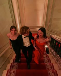 three young women walking down the stairs in red dresses and black tuxedo suits