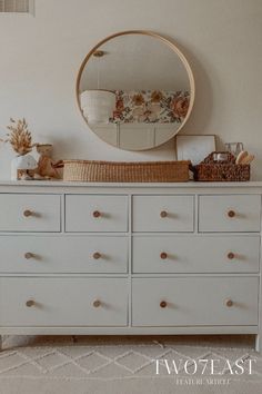 a white dresser with drawers and a round mirror above it on top of the dresser