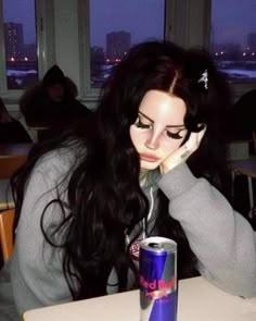 a woman sitting at a table with a can of soda in front of her face