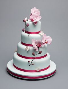 a three tiered white cake with pink flowers on the top and red stripes down the side