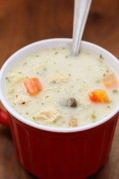 a red cup filled with soup sitting on top of a wooden table next to a white spoon