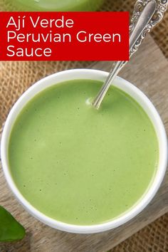 two bowls filled with green sauce on top of a wooden table next to a spoon