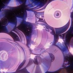 many cds are stacked on top of each other in the middle of an image with blue and purple hues