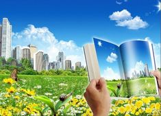 a person is holding an open book in front of a field with yellow flowers and skyscrapers