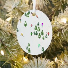 a white ornament hanging from a christmas tree decorated with skiers and trees