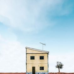 a small building sitting on top of a dry grass field next to a lone tree